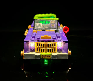 Purple and yellow LEGO Joker lowrider car with illuminated headlights, grille, roof, and undercarriage lights against black b
