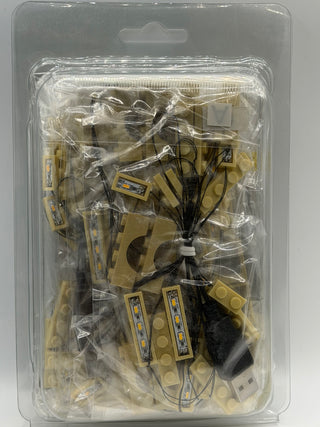 LED lighting kit in clear blister packaging containing tan LEGO bricks with embedded lights, wiring, and a power adapter.