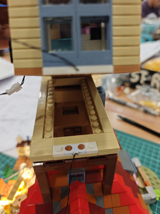 Tan and brown building model with white power connector and red LED lights on base.