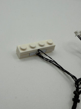 White connector block with four circular mounting points and black wired leads attached.