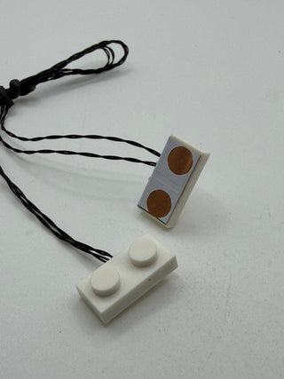 Two vertical power connectors with dual copper contacts, one gray and one white, connected by black wire cord.
